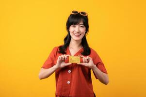portret jong mooi Aziatisch vrouw gelukkig glimlach gekleed in oranje kleren tonen credit kaart geïsoleerd Aan geel achtergrond. betalen en aankoop boodschappen doen betaling concept. foto