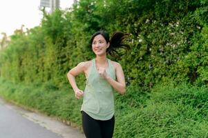 fit Aziatisch jong vrouw jogging in park glimlachen gelukkig rennen en genieten van een gezond buitenshuis levensstijl. vrouw jogger. geschiktheid loper meisje in openbaar park. gezond levensstijl en welzijn wezen concept foto