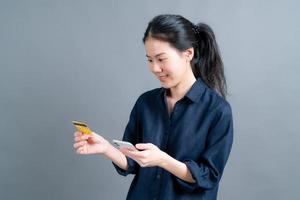 jong Aziatisch meisje dat een plastic creditcard toont terwijl ze een mobiele telefoon vasthoudt foto