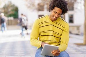zwarte man met behulp van een digitale tablet zittend op een bankje buiten. foto