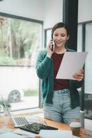 gelukkig zakenvrouw pratend Aan mobiel telefoon terwijl analyseren wekelijks schema in haar notebook. foto