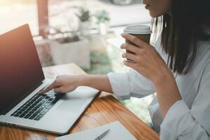 dichtbij omhoog, bedrijf vrouw hand- Holding kop en drinken koffie en gebruik makend van laptop, aan het kijken video, film of webinar, nemen breken foto