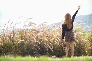 een jong vrouw in een lang mouwen zwart overhemd en kort rok gelukkig verhoogt haar handen bovenstaand haar hoofd na verkennen natuur en gras veld- in de avond omdat de lucht is vers. kopiëren ruimte voor tekst foto