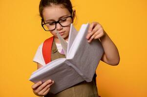 slim elementair leerling kind meisje vervelend bril, leert lezing alfabet, Holding mockup boek, geïsoleerd Aan oranje foto
