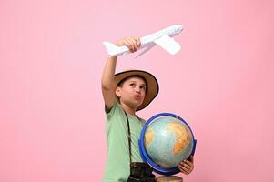 een schattig jongen houdt een wereldbol en een vliegtuig in zijn handen, simuleren een vlucht in de omgeving van de wereldbol. reizen concept. foto