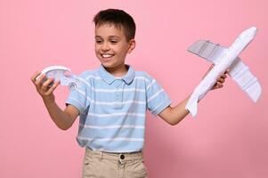 een knap schooljongen met een papier auto- en een vliegtuig in zijn handen, kiezen welke vervoer is het beste voor reizend. voordelen van land- en lucht vervoer foto