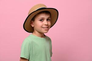 kant portret van een knap schooljongen in zomer rietje hoed, op zoek Bij camera en staand geïsoleerd over- roze achtergrond met kopiëren ruimte. detailopname foto