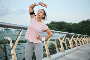 jong geschiktheid vrouw werken uit buitenshuis Aan de brug. sport- Dames in sportkleding uitrekken haar lichaam in de vroeg ochtend- Bij zonsopkomst Aan de rivier- kust. sport, motivatie, gezond levensstijl concept foto