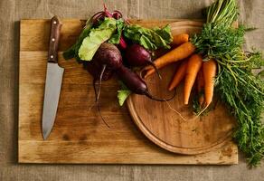 vlak leggen. seizoensgebonden rauw groenten. trossen van vers biologisch bieten, baby wortels met tops en keuken mes Aan een houten snijdend bord. veganistisch voedsel achtergrond foto