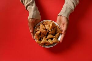 vlak leggen . handen Holding een heerlijk en zoet bord vol van vers traditioneel Marokkaans handgemaakt snoepgoed, geïsoleerd Aan rood achtergrond. foto