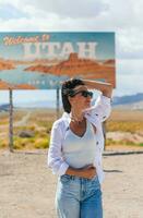 mooi vrouw Aan haar reis door de auto. Welkom naar Utah weg teken. groot Welkom teken groeten reist in monument vallei, Utah foto