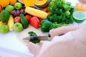 handen met een mes die groente hakt over een houten snijplank op de tafel bij een witte gordijnachtergrond foto