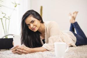 aantrekkelijke jonge Indiase vrouw ontspannen met mobiel thuis. foto