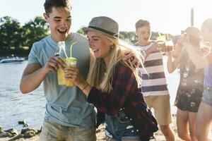 groep van gelukkig vrienden wandelen Bij de rivieroever roosteren met drankjes foto