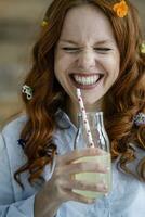 portret van lachend roodharige vrouw met bloesems in haar- drinken limonade foto