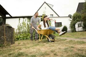 speels Mens voortvarend vrouw zittend in kruiwagen in tuin foto