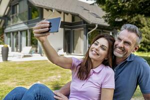 gelukkig paar zittend in tuin van hun huis nemen een selfie foto