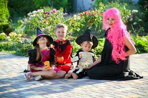 jong kinderen truc of behandelen gedurende halloween . kinderen en een vrouw zijn zittend Aan de weg in halloween kostuums. foto