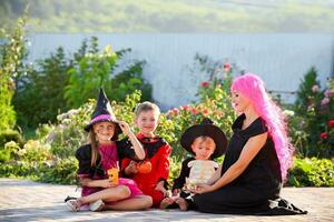 jong kinderen truc of behandelen gedurende halloween . kinderen en een vrouw zijn zittend Aan de weg in halloween kostuums. foto