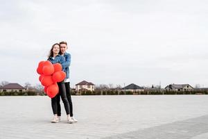 jonge verliefde paar met rode ballonnen omarmen en zoenen buitenshuis foto