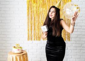 vrouw in verjaardagshoed met ballon op gouden achtergrond holding foto