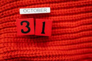 houten kubus kalender tonen oktober 31, halloween geïsoleerd Aan rood achtergrond rood gebreid trui. foto
