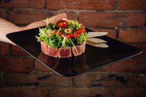 tonijn tartaar geserveerd met geroosterd brood en salade Aan zwart steen bord foto