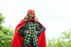 Aan een mooi dag in de park, een jong meisje geniet haar vakantie. speels met een rood superheld kostuum en masker. foto