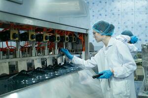 vrouw wetenschapper in wit jas en blauw hoed werken in de controle machine van productie lijn. foto