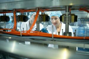 vrouw wetenschapper in wit jas en blauw hoed werken in de controle machine van productie lijn. foto