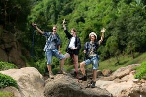 jong Mens wandelaar met rugzak en trekking polen met een jong Mens helpen naar Trekken hem omhoog naar staan Aan de rots foto