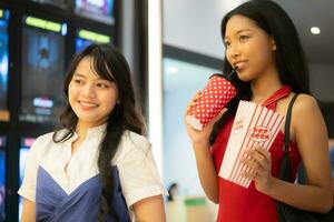 jong Aziatisch vrouw staand in lijn naar kopen film kaartjes en in hand- popcorn en drinken foto