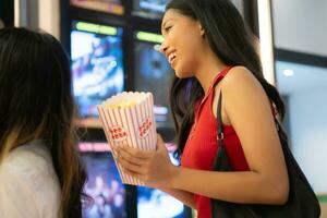 jong Aziatisch vrouw staand in lijn naar kopen film kaartjes en in hand- popcorn en drinken foto