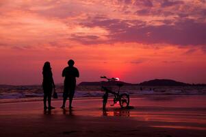 silhouet van paar met fiets Aan de strand Bij zonsondergang foto