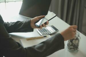 besparing geld en accounting concept. bedrijf Mens zetten munt insert naar pot en maken boekhouden boek voor financiën beheer naar investering en besparing. foto