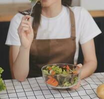 heerlijk fruit en groenten Aan een tafel en vrouw Koken. huisvrouw is snijdend groen komkommers Aan een houten bord voor maken vers salade in de keuken. foto