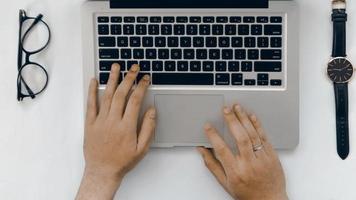 bovenaanzicht hand van laptop, bril en horloge op witte achtergrond foto