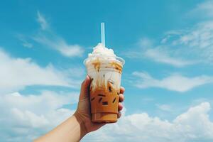 hand- Holding bevroren koffie in een plastic kop met een blauw lucht en wolk achtergrond. ai gegenereerd foto