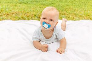 schattig weinig pasgeboren meisje aan het liegen Aan buik Aan deken in gazon Aan zonnig zomer dag buitenshuis. zuigeling hebben pret buitenshuis. zuigeling baby kind resting spelen aan het leren naar kruipen. moederschap gelukkig kind concept. foto