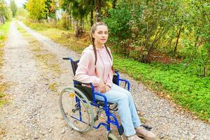 jong gelukkig handicap vrouw in rolstoel Aan weg in ziekenhuis park aan het wachten voor geduldig Diensten. verlamd meisje in ongeldig stoel voor gehandicapt mensen buitenshuis in natuur. revalidatie concept. foto