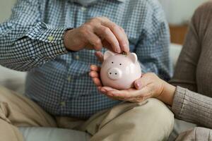 besparing geld investering voor toekomst. senior volwassen volwassen paar handen zetten geld munt in varkentje bank. oud Mens vrouw tellen besparing geld planning pensioen begroting besparing investering bank concept foto