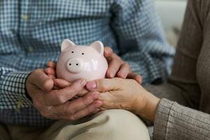 besparing geld investering voor toekomst. senior volwassen volwassen paar handen Holding varkentje bank met geld munt. oud Mens vrouw tellen besparing geld planning pensioen begroting. investering bank concept. foto