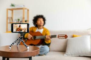 blogger gitarist. Afrikaanse Amerikaans meisje blogger spelen gitaar pratend naar webcam opname vloggen. sociaal media influencer vrouw streaming Bij huis binnenshuis. muziek- inhoud Schepper uitzending zelfstudie. foto