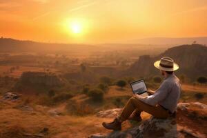 digitaal nomade zittend Aan top van een heuvel werken met zijn laptop over- de stad Bij zonsondergang ,generatief ai. foto