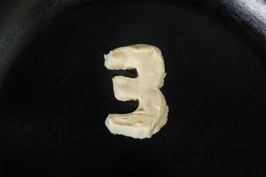 boter in de vorm van nummer 3 op hete pan - close-up bovenaanzicht foto