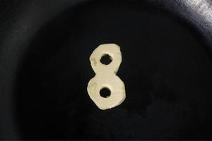 boter in de vorm van nummer 8 op hete pan - close-up bovenaanzicht