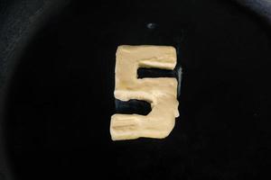 boter in de vorm van nummer 5 op hete pan - close-up bovenaanzicht