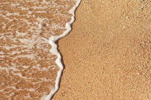 strandzand zeekust met golf en witte schuimige zomerachtergrond foto