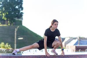 jong, fit en sportief meisje in zwart kleren uitrekken na de training in de buurt de openbaar fontein in de stedelijk stad park. foto