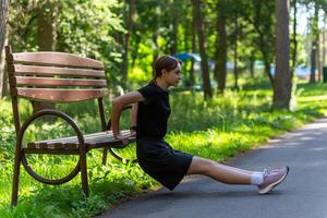 mooi jong sportief vrouw in zwart t-shirt, zwart shorts en roze trainers opwarming omhoog oefenen triceps foto